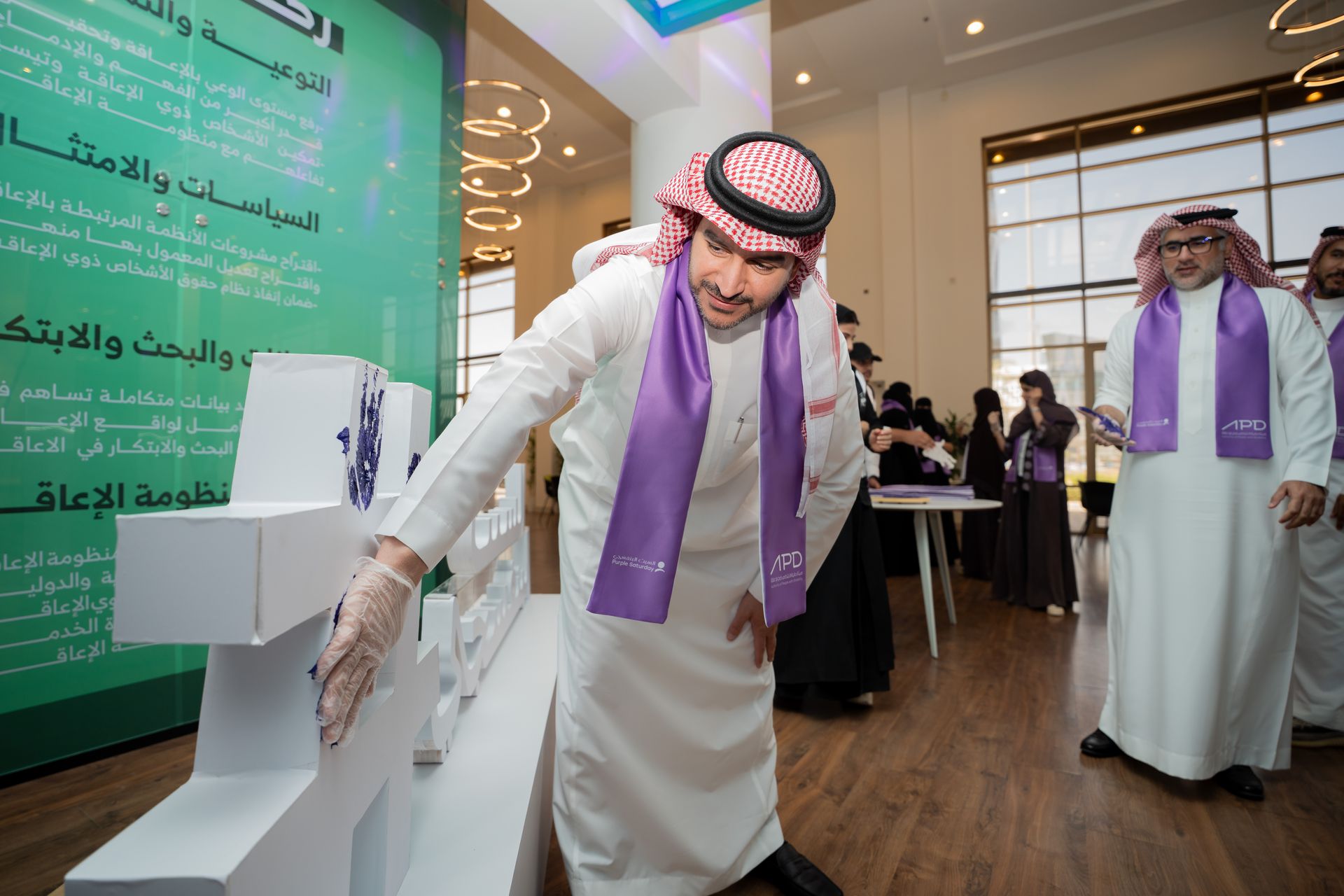 يظهر بالصورة سعادة نائب الرئيس للتواصل والتمكين خلال مشاركته فعالية البصمة البنفسجية على مجسم اسم المبادرة