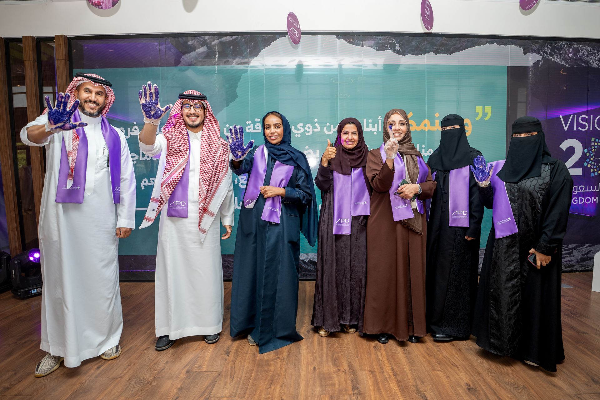 يظهر بالصورة عدد من منسوبي الهيئة خلال مشاركتهم فعالية البصمة البنفسجية على مجسم اسم المبادرة
